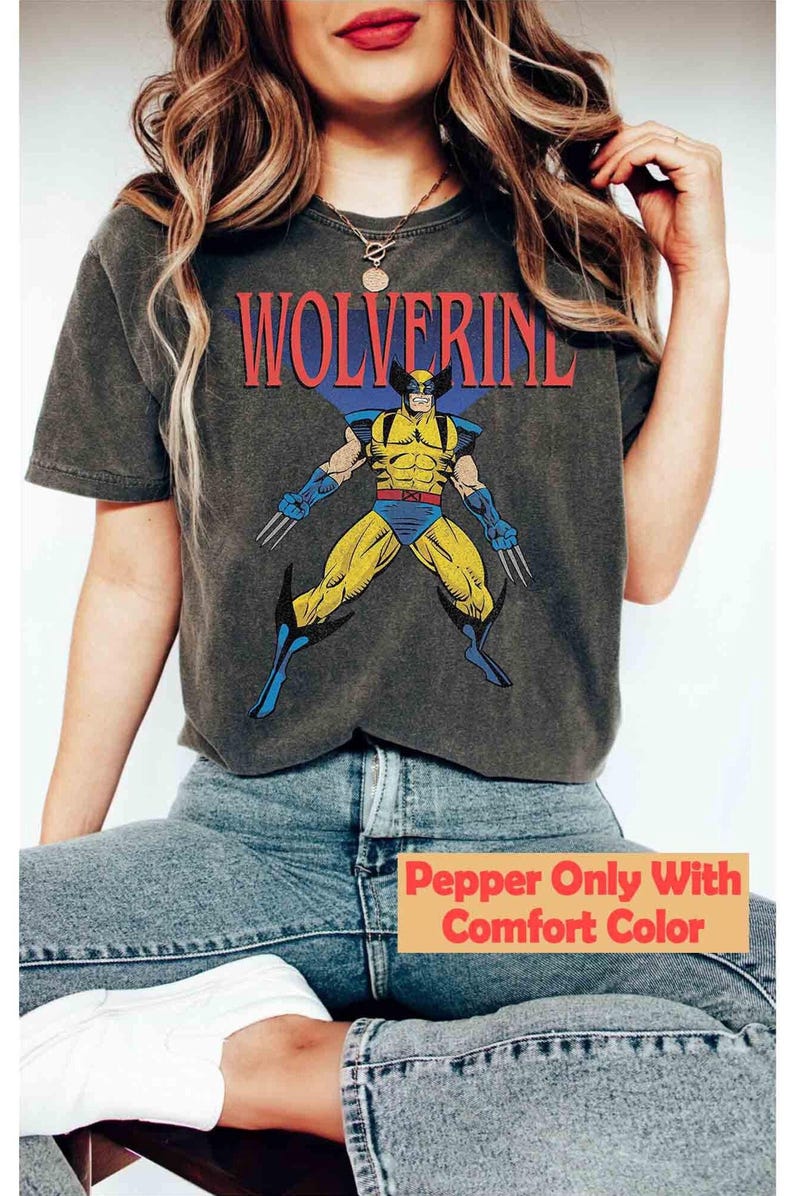 May include: A charcoal gray short-sleeve t-shirt featuring a graphic print of the comic book character Wolverine in a yellow and blue suit with metal claws. The word WOLVERINE is printed in red capital letters above the character illustration.