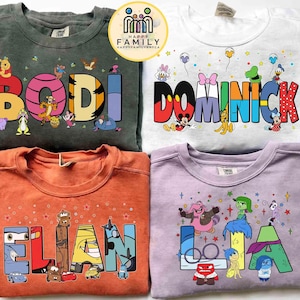 May include: Four crewneck sweatshirts in various colors, each featuring a name in colorful block letters with cartoon character illustrations. The names are "BODI", "DOMINICK", "ELIAN", and "LA". The sweatshirts are from the "Happy Family" brand.