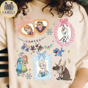 Op de afbeelding: Een beige t-shirt met een grafische print van personages uit Frozen, waaronder Anna, Elsa, Olaf, Sven en Bruni. Het ontwerp bevat hart- en ovaalvormige kaders, een banner met de tekst Frozen en sneeuwvlokaccenten in roze en blauw.