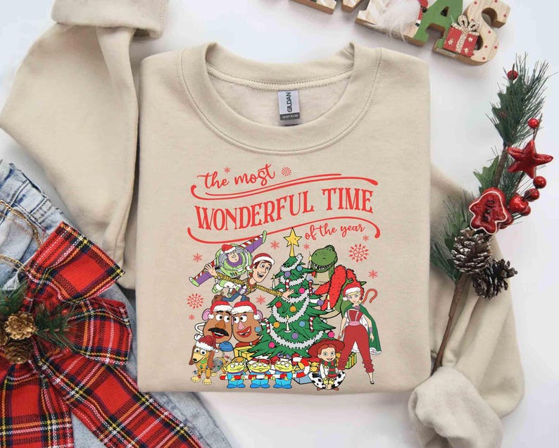 May include: Beige sweatshirt with a festive graphic featuring characters from a popular animated movie. The text "the most WONDERFUL TIME of the year" is printed in red. A Christmas tree and snowflakes are also included in the design.
