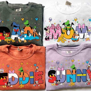 May include: Four crewneck sweatshirts in various colors, each featuring a Disney-themed design. The sweatshirts display the words "DAD", "MOM", "EDDIE", and "SUNNY" with Disney characters and balloons.