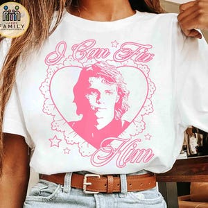 May include: White t-shirt with a pink graphic. The graphic features a portrait inside a heart-shaped frame with the text "I Can Fix Him". The design includes stars and decorative elements.