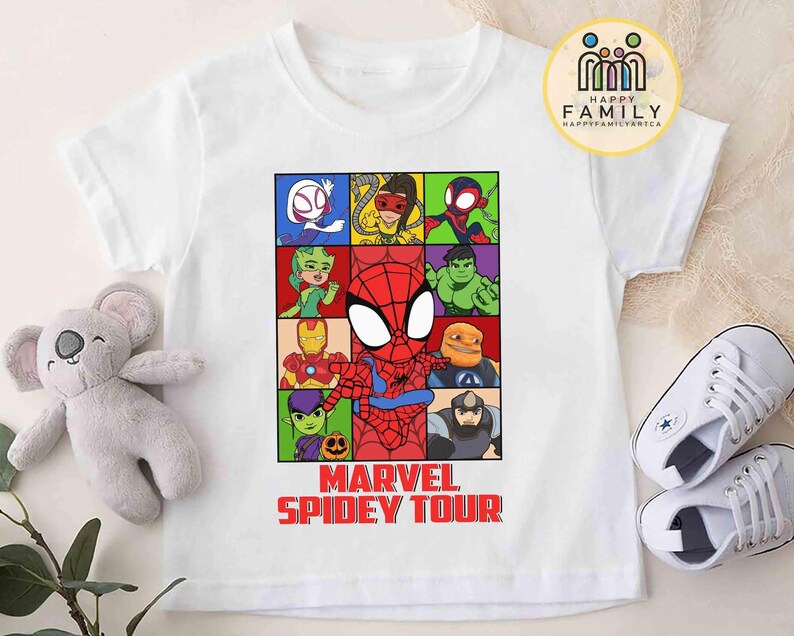 May include: White t-shirt featuring a colorful graphic of Spider-Man and other Marvel characters in a grid. The text "MARVEL SPIDEY TOUR" is printed in red below the grid. A plush koala and white sneakers are next to the shirt.
