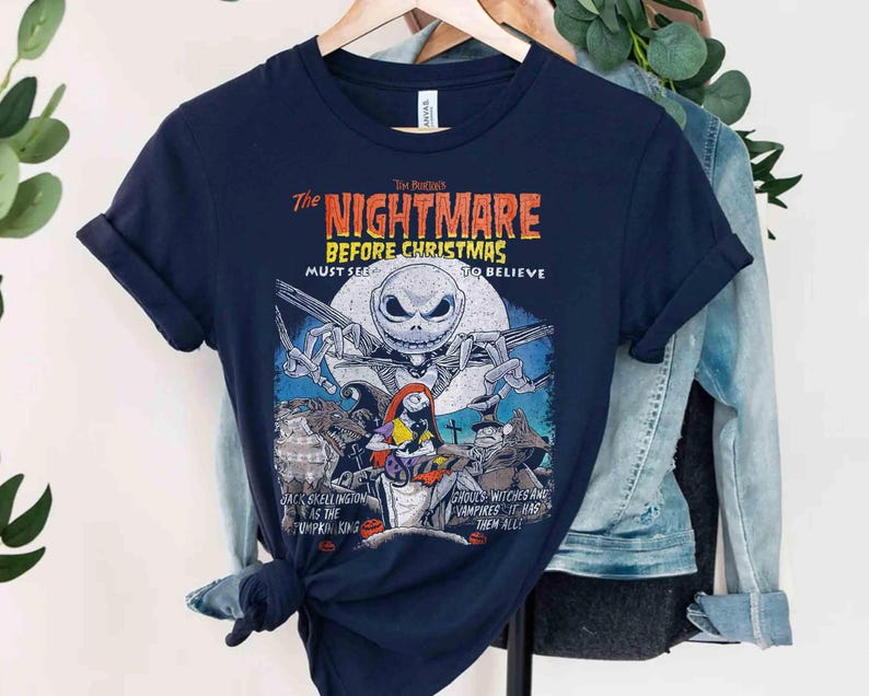 May include: A navy blue short-sleeve t-shirt featuring a graphic print from The Nightmare Before Christmas. The design includes Jack Skellington, Sally, and other characters with the text The Nightmare Before Christmas, Must See To Believe.