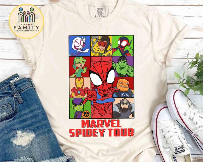 May include: Cream-colored t-shirt featuring a colorful grid of Marvel characters, including Spider-Man. The shirt has the text "MARVEL SPIDEY TOUR" in red. The shirt is paired with blue denim shorts and white sneakers.