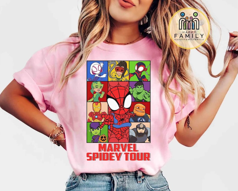 May include: Pink t-shirt featuring a colorful graphic of Marvel characters, including Spider-Man, Iron Man, and Hulk. The design is set in a grid pattern with the text "MARVEL SPIDEY TOUR" in red at the bottom. The shirt has short sleeves.