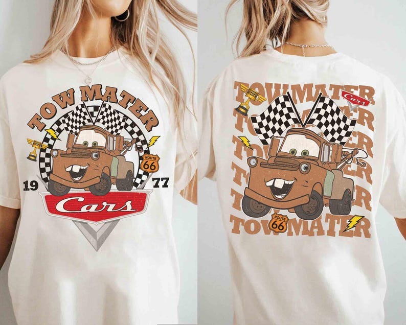 May include: Cream-colored t-shirt featuring a cartoon image of Tow Mater from the movie Cars. The design includes the text "Tow Mater," a checkered flag, and the Route 66 logo. The front and back of the shirt are visible.