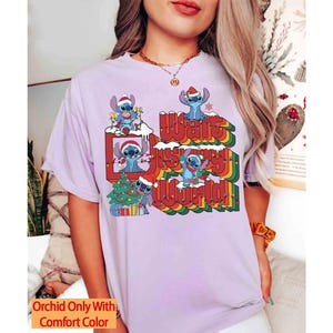 K&ouml;nnte beinhalten: Helllila T-Shirt mit einem Aufdruck von Stitch mit Weihnachtsm&uuml;tzen und dem Text "Walt Disney World!" in einem Retro-Regenbogen-Design. Das Shirt hat auch den Text "Orchid Only With Comfort Color".