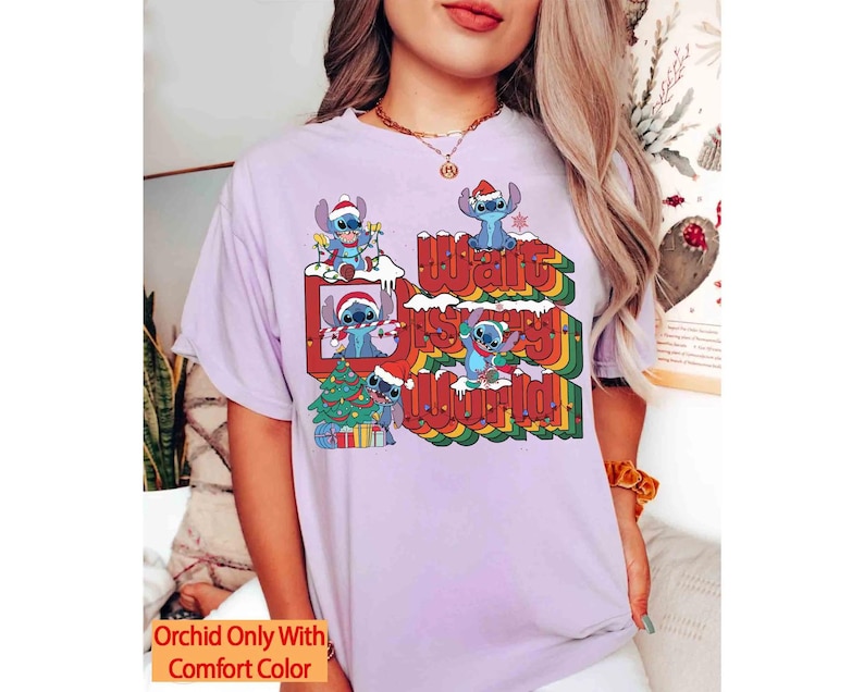 K&ouml;nnte beinhalten: Helllila T-Shirt mit einem Aufdruck von Stitch mit Weihnachtsm&uuml;tzen und dem Text "Walt Disney World!" in einem Retro-Regenbogen-Design. Das Shirt hat auch den Text "Orchid Only With Comfort Color".