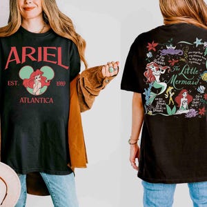 Puede incluir: Una camiseta negra con un gr&aacute;fico frontal que incluye el texto rojo ARIEL, EST. 1989, ATLANTICA y una ilustraci&oacute;n circular de Ariel. El gr&aacute;fico trasero muestra el texto The Little Mermaid, Ariel, Flounder e ilustraciones marinas.