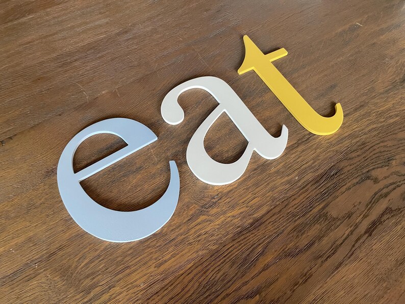 May include: The word "eat" spelled out in three dimensional letters. The letter "e" is light blue, the letter "a" is white, and the letter "t" is yellow.