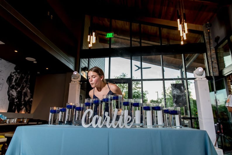 May include: A young person blows out candles on a table decorated with blue and white candles and the name "Carlie" in white letters.