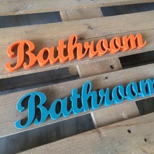 May include: Two wooden signs spelling out the word "Bathroom" in a cursive font. The top sign is painted orange and the bottom sign is painted teal.