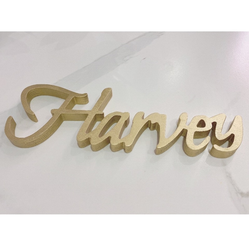 May include: Gold layered wooden name sign spelling "Harvey".