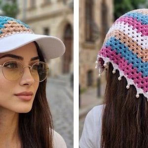 May include: A crochet head covering featuring a white solid brim and a multi-colored chevron pattern in shades of pink, blue, and tan. The triangular back section is finished with a white scalloped edge adorned with small white beads.