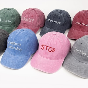 Puede incluir: Una colección de gorras de béisbol en varios colores, incluyendo verde, rojo, azul y rosa. Cada gorra presenta texto bordado, como "1 mom", "BRAUT", "YOUR NAME", "STOP" y "Custom Embroidery".