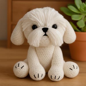 Può includere: Un cane bianco all'uncinetto fatto a mano con occhi e naso neri. Il cane ha orecchie flosce e un viso soffice, con dettagli neri cuciti sulle zampe. Il cane è seduto su una superficie di legno.