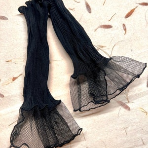 Pu&ograve; includere: Un paio di maniche in tulle nero con un bordo arricciato e una sovrapposizione di tulle nero.