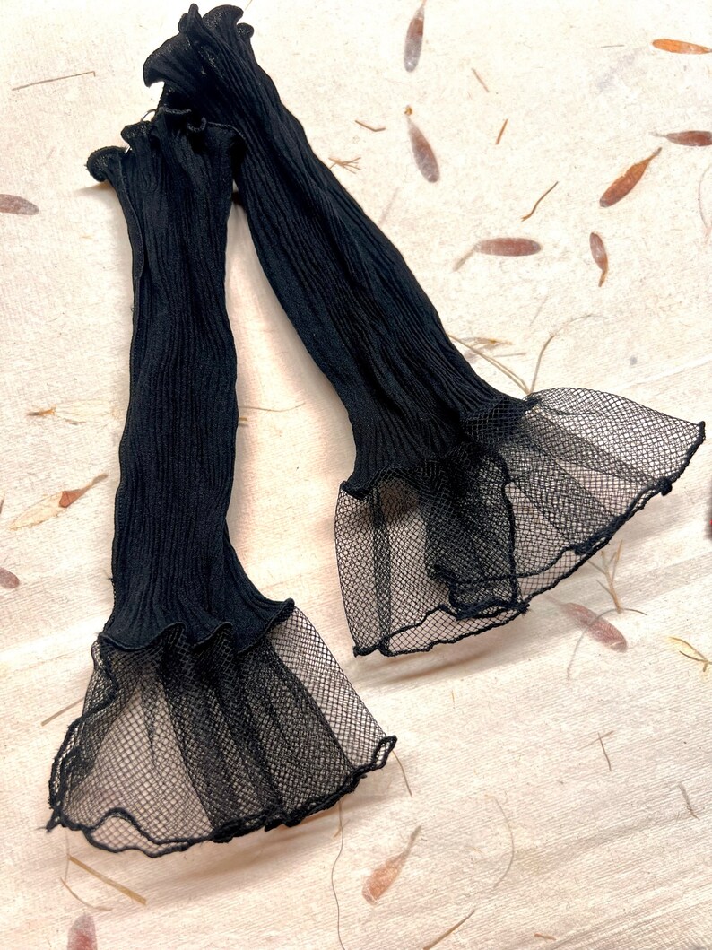 Pu&ograve; includere: Un paio di maniche in tulle nero con un bordo arricciato e una sovrapposizione di tulle nero.