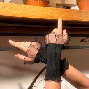 Pu&ograve; includere: Un paio di polsini neri in rete con bordi arricciati. I polsini sono realizzati in tessuto elastico e hanno un aspetto delicato e trasparente.
