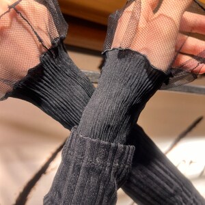 Pu&ograve; includere: Maglia nera a maniche lunghe con dettagli di volant in rete nera ai polsini.