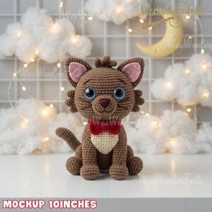 May include: A brown crocheted cat toy with large blue eyes, pink inner ears, a cream-colored chest patch, and a red bow tie. The cat is sitting upright and measures 10 inches in height as indicated by the text at the bottom of the image.