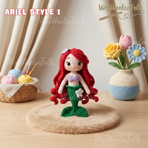 May include: Ariel Style 1 crochet doll with red hair, a purple top, and a green tail. The doll is displayed on a brown surface. A woven basket with yarn and a crochet hook is in the background. The text "We Woolen Folk" is visible.
