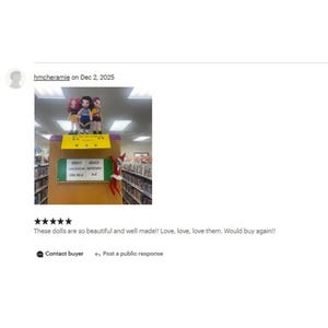 Op de afbeelding: Drie kleine poppen in kleurrijke outfits staan op een boekenplank in een bibliotheek. Op de plank staat "ADULT FICTION MYSTERY". Een elfdecoratie is zichtbaar. De afbeelding bevat een klantbeoordeling.