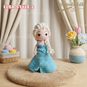 May include: A handmade crochet doll in the style of Elsa, with a light blue dress and a long, white braid. The doll is standing on a brown rug. The text "ELSA STYLE 2" is visible in the upper left corner.