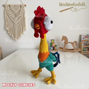 May include: A handmade crochet rooster toy, approximately 12 inches tall. The rooster features a red comb, yellow neck, and blue and green body. The eyes are white with black pupils. The toy is standing on a white surface.