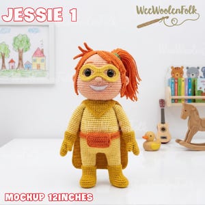 Puede incluir: Mu&ntilde;eca de ganchillo llamada Jessie, de aproximadamente 30 cm de altura, vestida de superh&eacute;roe. La mu&ntilde;eca tiene pelo naranja, una m&aacute;scara amarilla y un atuendo amarillo y naranja. La mu&ntilde;eca est&aacute; de pie frente a un fondo blanco.