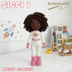 Puede incluir: Mu&ntilde;eca de ganchillo con un traje de astronauta blanco con detalles rosas, incluyendo botas y guantes. La mu&ntilde;eca tiene pelo rizado marr&oacute;n y un tono de piel a juego. La mu&ntilde;eca mide aproximadamente 30 cm de altura.