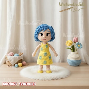 May include: A handmade crochet doll with blue hair and a yellow dress adorned with blue flower accents. The doll is approximately 12 inches tall and stands on a white faux fur rug. The text "MOCKUP 12INCHES" is visible at the bottom.