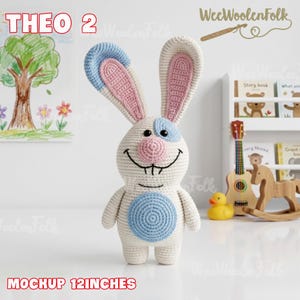 Puede incluir: Un juguete de conejo tejido a mano, de aproximadamente 30 cm de altura. El conejo tiene un cuerpo blanco con detalles azules y rosas en las orejas y la cara. Presenta un c&iacute;rculo azul en el vientre y una cara sonriente. El texto "THEO 2" y "MOCKUP 12INCHES" son visibles.