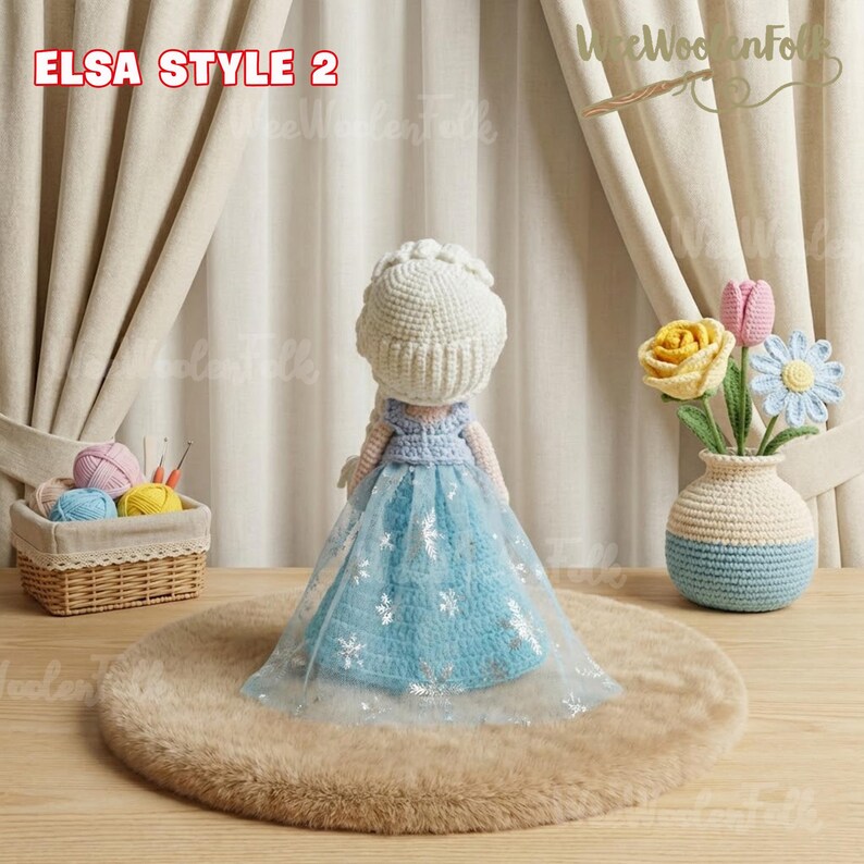 May include: A handmade crochet doll in the style of Elsa from Frozen, wearing a blue dress with silver snowflake accents and a white crown. The doll is displayed on a brown rug, with the text "ELSA STYLE 2" visible. A crochet vase with flowers is in the background.
