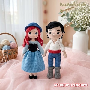 May include: Two handmade crochet dolls, one resembling a princess with red hair and a blue dress, the other a prince in a white shirt and blue pants. The dolls are approximately 12 inches tall. The dolls are displayed on a pink surface.