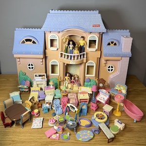May include: A large Fisher-Price dollhouse with a blue roof and tan walls, featuring a balcony with five plastic dolls. The set includes numerous miniature furniture pieces, including chairs, tables, a bathtub, a toilet, and various household accessories.