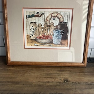 Può includere: Stampa incorniciata con un'illustrazione stravagante di omini di pan di zenzero, una ghirlanda e vari oggetti da cucina. L'opera d'arte include una figura con un telescopio, una ciotola di bacche rosse e una brocca blu. La cornice è in legno.