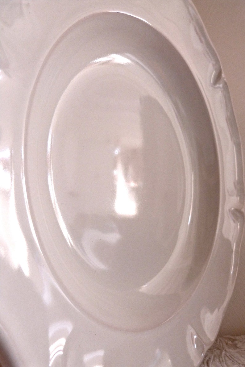 May include: A white ceramic plate with a scalloped edge. The plate has a wide rim and a slightly recessed center. The surface is smooth and glossy, reflecting light. The plate is likely for serving food.
