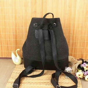 May include: A black backpack with a woven texture and leather accents. The bag features adjustable straps, a top handle, and a drawstring closure. The bottom of the backpack is made of solid black leather. The bag is designed for everyday use.