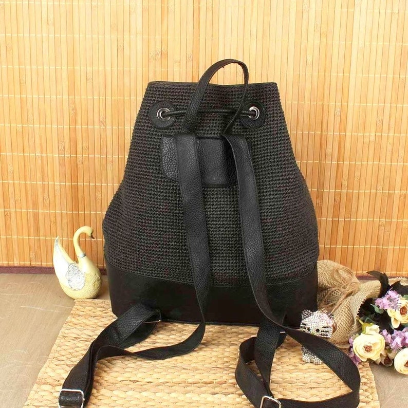 May include: A black backpack with a woven texture and leather accents. The bag features adjustable straps, a top handle, and a drawstring closure. The bottom of the backpack is made of solid black leather. The bag is designed for everyday use.