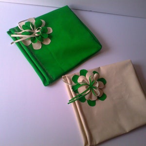 May include: Two square gift boxes, one green and one beige, each adorned with a decorative flower. The flowers feature green and cream-colored petals and ribbon accents, adding a touch of elegance to the wrapped presents.