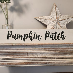 May include: White wooden sign with black cursive lettering that reads "Pumpkin Patch". The sign is sitting on a white shelf with a white, distressed, five-pointed star behind it.