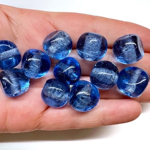 May include: A collection of eleven small, rounded glass beads in a vibrant translucent blue color. Each bead features a distinct, textured white band running through the center, creating a contrast against the smooth, polished surface of the glass.