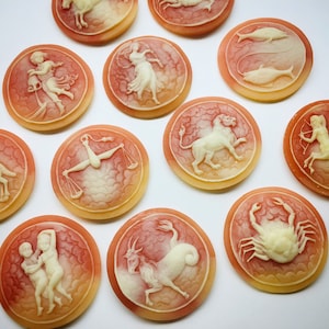 May include: Twelve round, cream-colored, zodiac signs with white carvings on a white background. Each sign is surrounded by a red and orange halo.