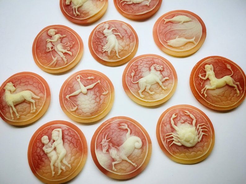 May include: Twelve round, cream-colored, zodiac signs with white carvings on a white background. Each sign is surrounded by a red and orange halo.