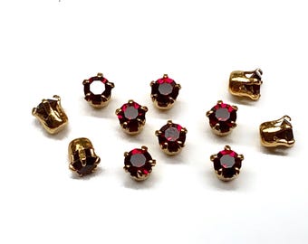 May include: Ten gold-toned metal settings with red rhinestone accents. The settings are round and have a prong setting for the rhinestones.