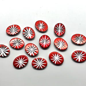 May include: A collection of 13 red oval-shaped buttons with a white starburst design.