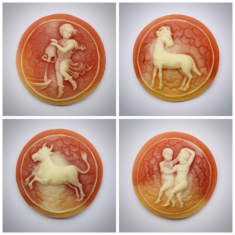 May include: Four round, cream-colored cameo pendants with zodiac symbols. The pendants are set in a red, orange, and yellow background with a cloud-like design. The symbols are Aquarius, Capricorn, Taurus, and Gemini.