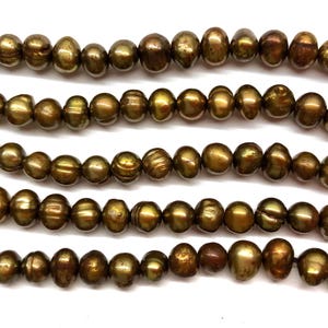 May include: Strands of olive-green freshwater pearls. The pearls have an irregular, oval shape and a lustrous finish. The beads vary in size and have a natural, organic appearance. Ideal for jewelry making.